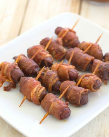 A white serving dish with bacon wrapped cocktail weenies.