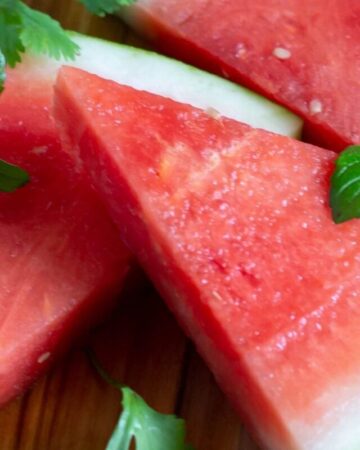 A triangle shaped watermelon slice on a cutting board.
