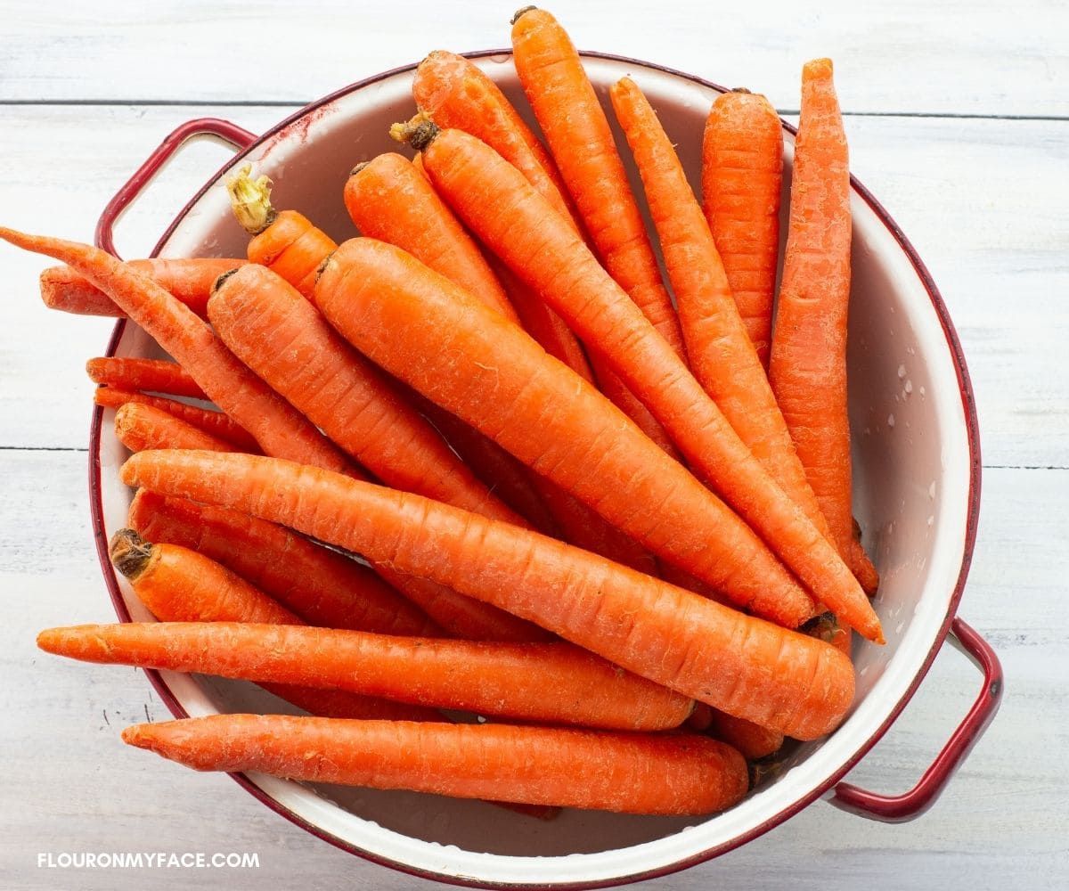 Fresh whole carrots in a white enamel colander.