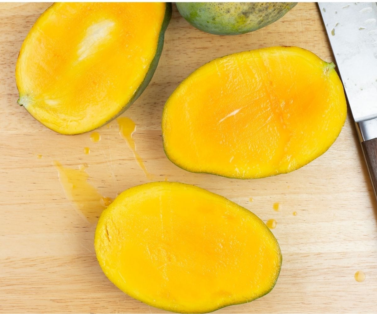 Fresh mangoes sliced in half on a cutting board.