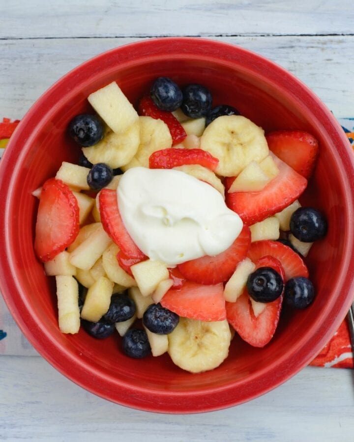 Fruit salad with crème fraiche in a red bowl.