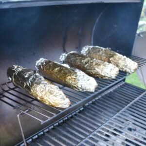 Corn on the cob wrapped in aluminum on a hot grill.