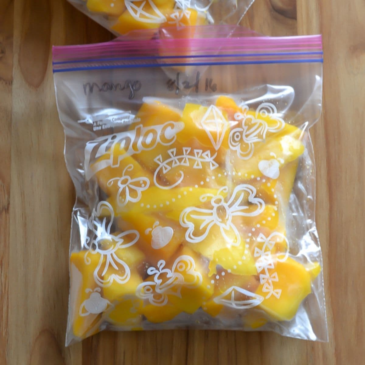 Cubed mango pieces in a freezer bag on a cutting board.