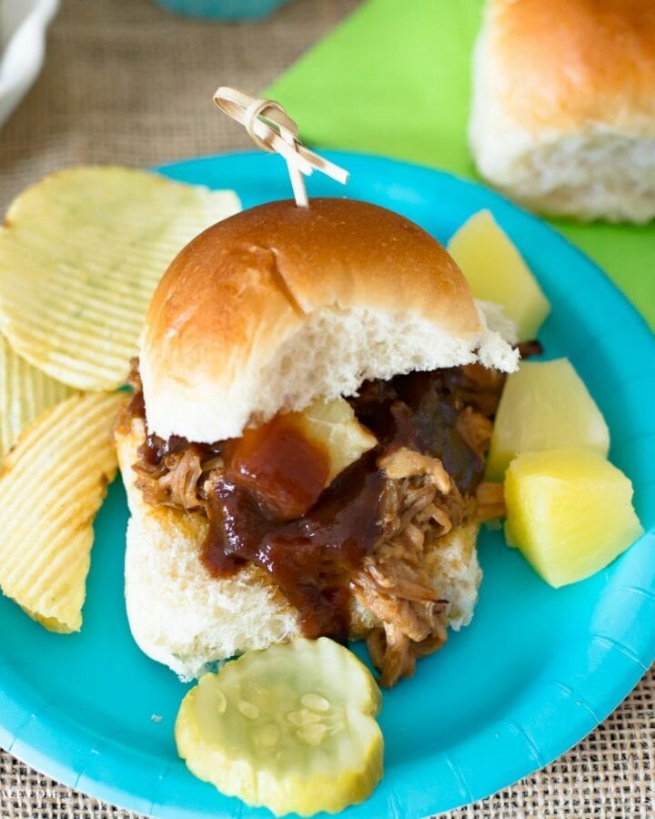 A pineapple pulled pork slider with chips and pineapple chunks on a plate.