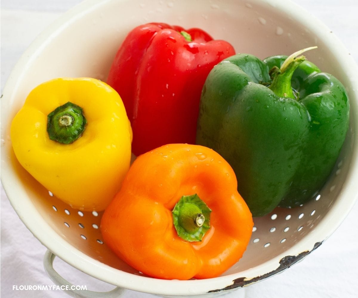 Four sweet bell peppers in a white enamel colander.