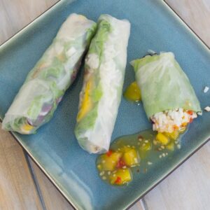 A plate of spring rolls with sweet chili mango sauce drizzled on the plate.