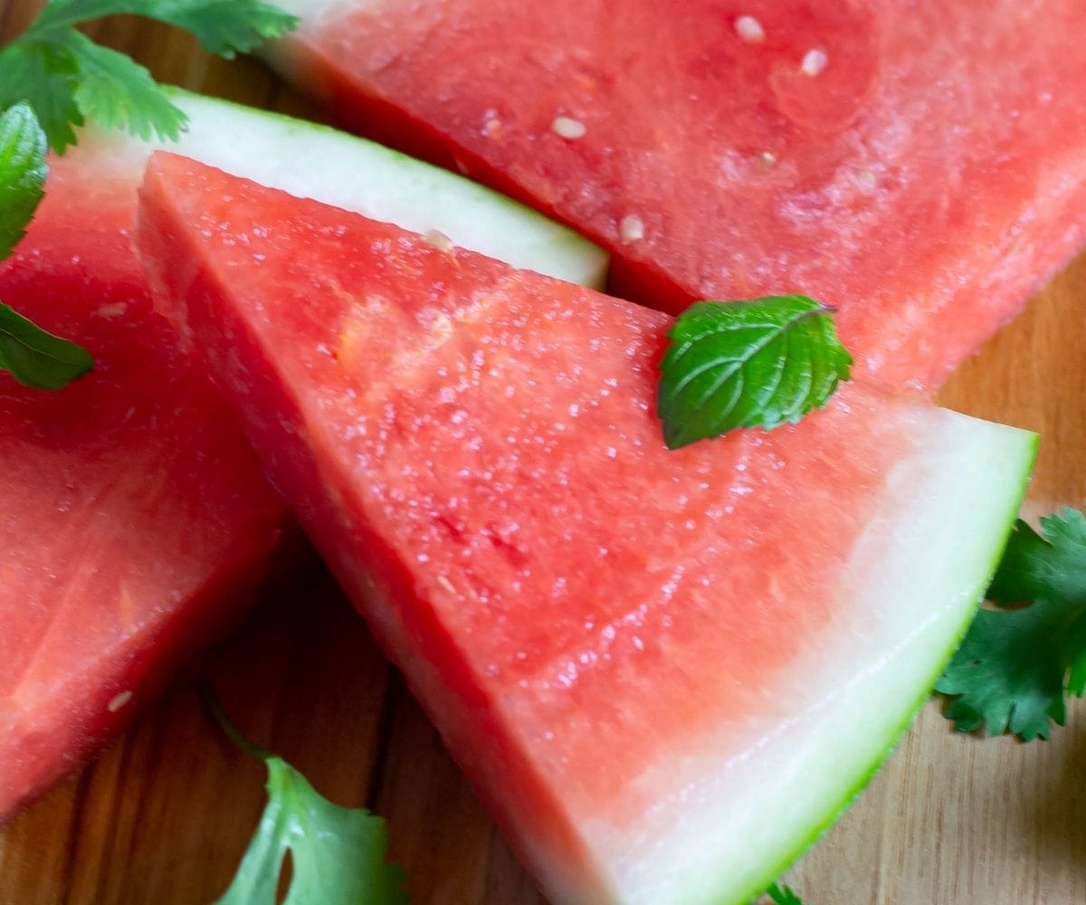 A triangle shaped watermelon slice on a cutting board.