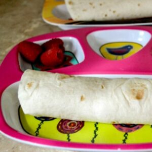 Child plate with a breakfast burrito and fruit for breakfast.