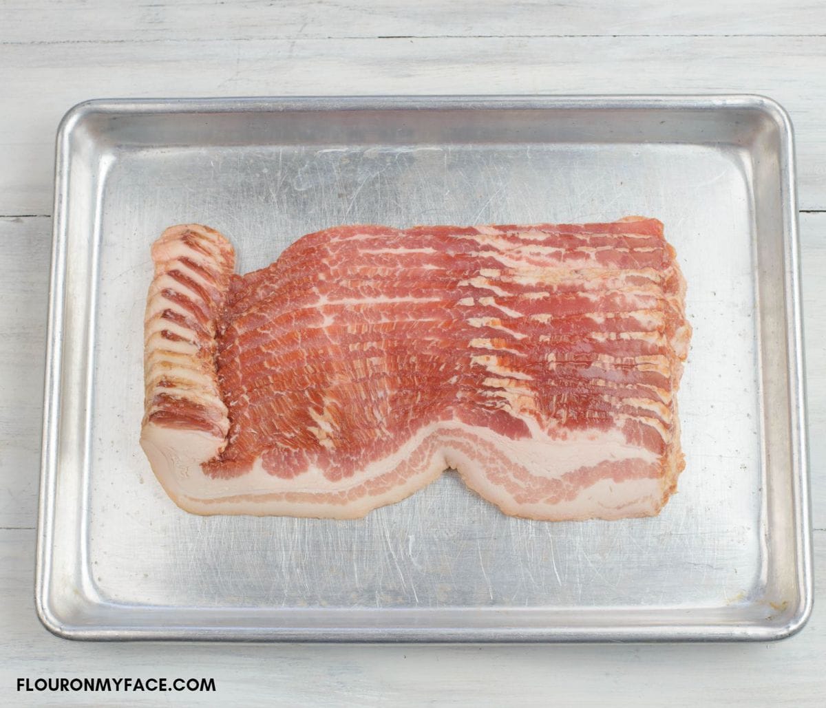 A 16 oz. package of opened bacon on a small baking sheet.