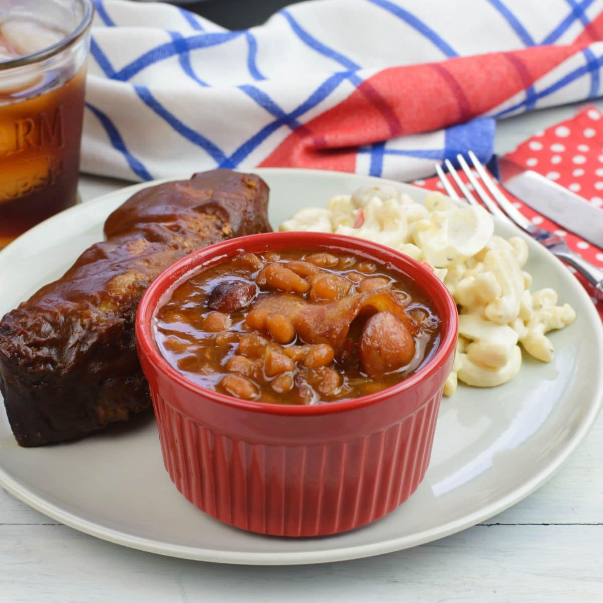 A small bowl filled with baked beans on a plate with ribs.