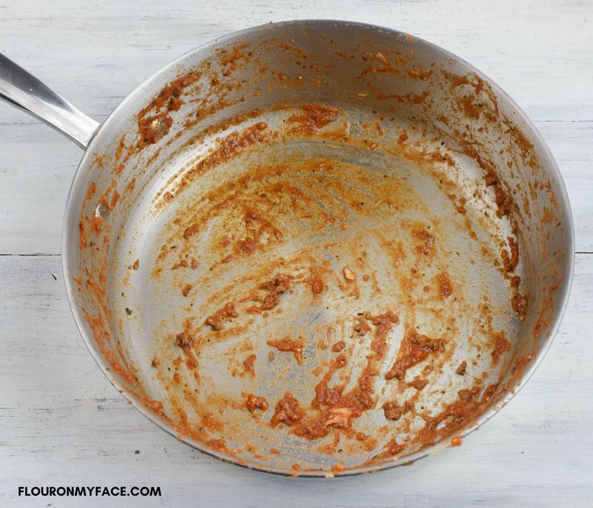 A large non stick skillet with pasta sauce coating the bottom and sides before washing.