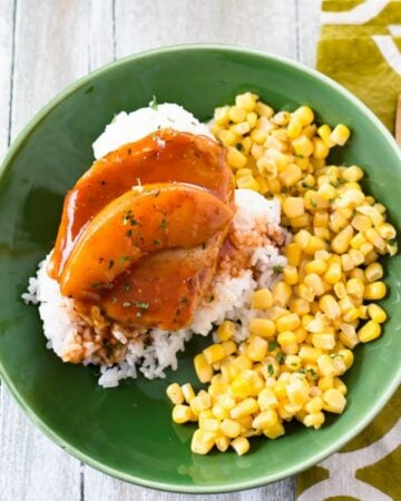 Peach Pork Chop served with white rice and corn on a green dinner plate.