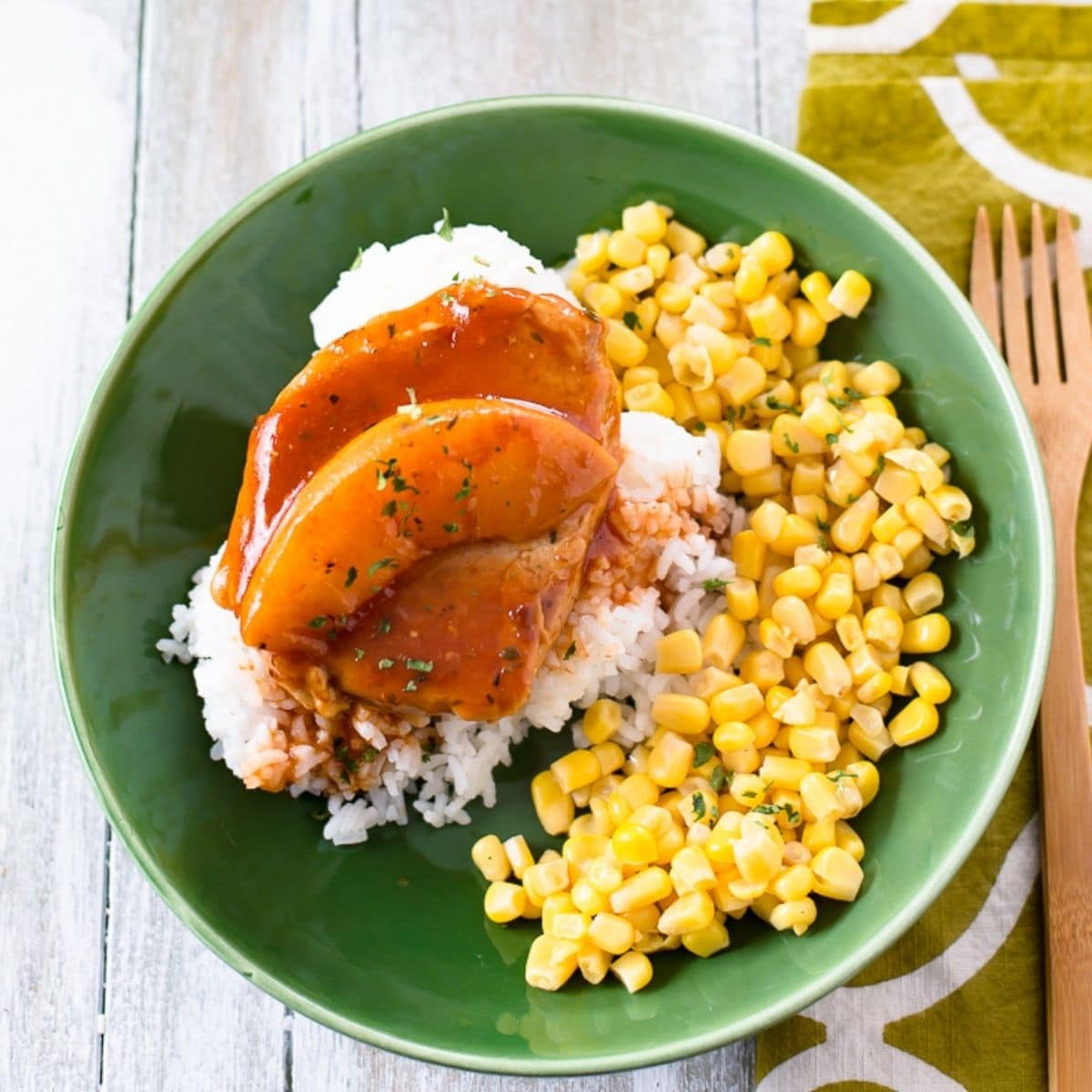 Peach Pork Chop served with white rice and corn on a green dinner plate.