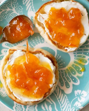 Toasted English Muffins with cream cheese and peach orange marmalade spread over the top on a teal glass plate.