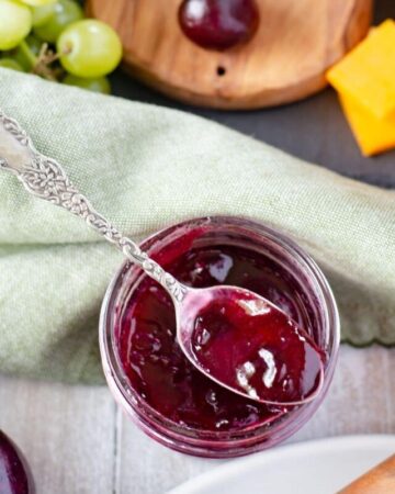 An opened canning jar of sweet cherry jam with a spoon across the top filled with jam.