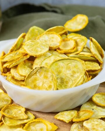 Dehydrated yellow squash chips in a white glass bowl.