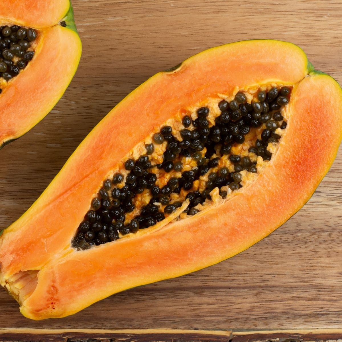 A large fresh papaya cut in half on a wooden cutting board.