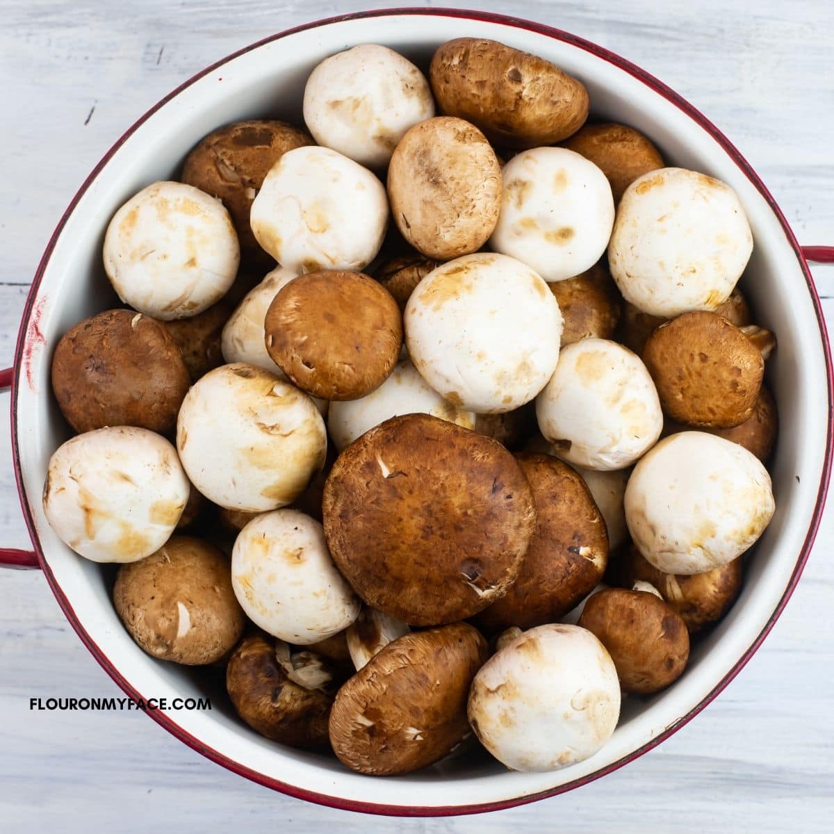 A white metal colander filled with white and baby portabella mushrooms.