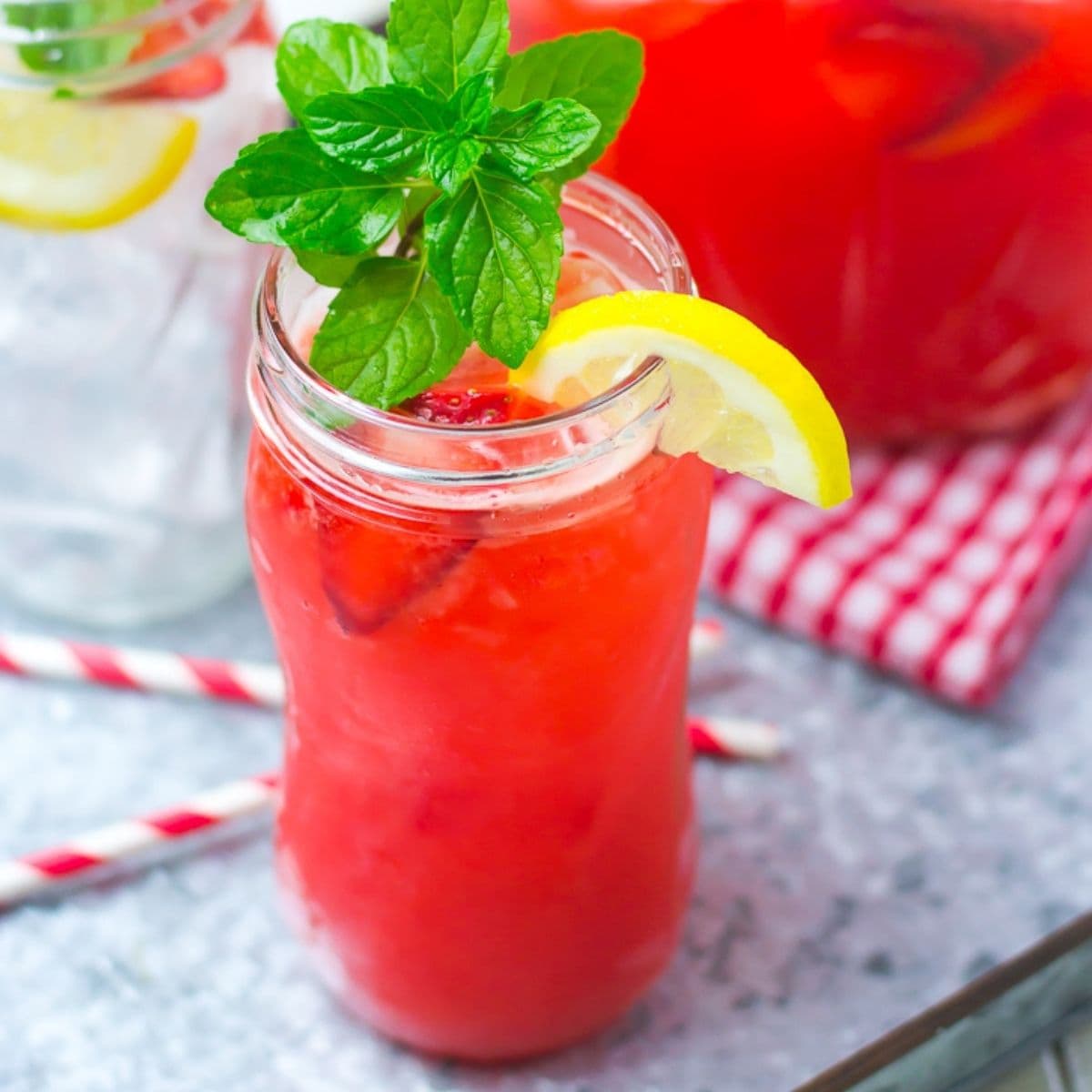 A glass jar filled with strawberry lemonade, with the filled pitcher in the background.