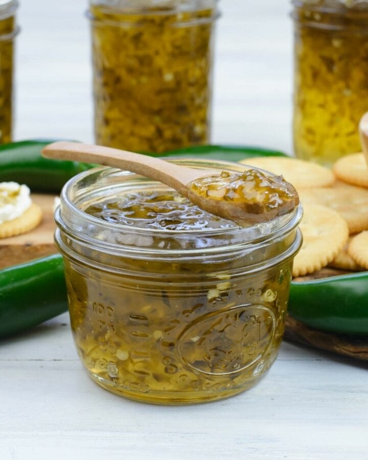 An open canning jar of Jalapeno Pepper Jelly with a spoon, more jars in the background.