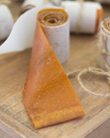 Homemade peach fruit leather roll ups on a wooden cutting board.