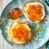 Toasted English Muffins with cream cheese and peach orange marmalade spread over the top on a teal glass plate.