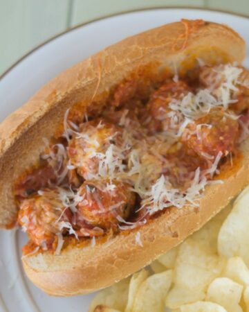 A Pepperoni Pizza Meatball Sub served with chips on a plate.