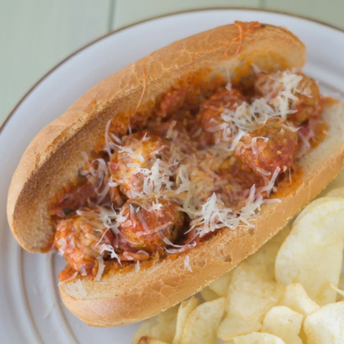 A Pepperoni Pizza Meatball Sub served with chips on a plate.