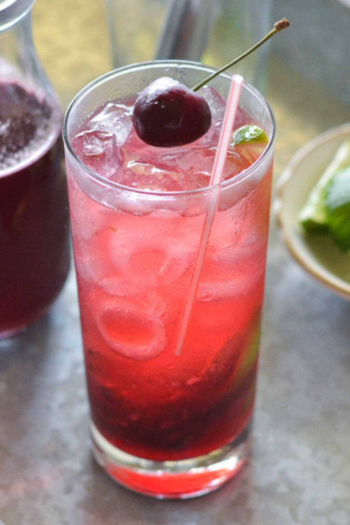 A tall glass on a galvanized metal tray filled with pomegranate cherry mojito.