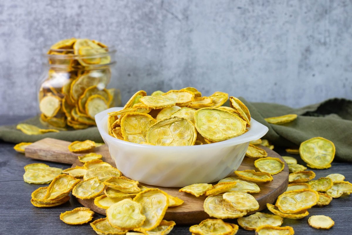 Dried sliced crookneck squash in a bowl with some scatter around on a table.