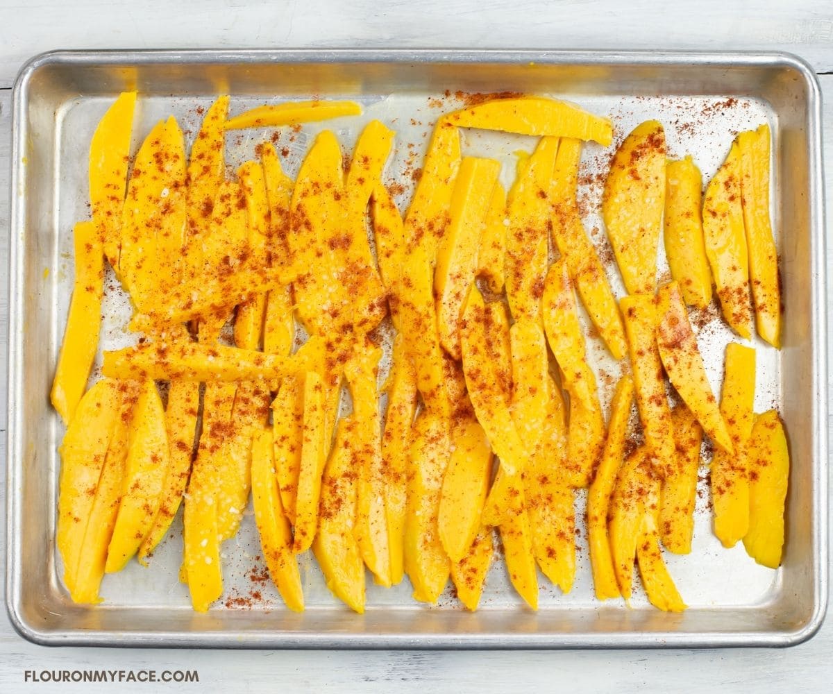 Sliced mango piece sprinkled with chili powder on a baking pan.