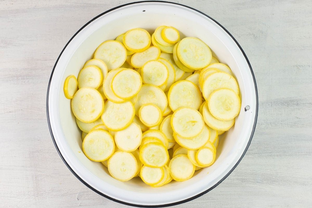 Sliced yellow crookneck squash in a white enamel bowl.