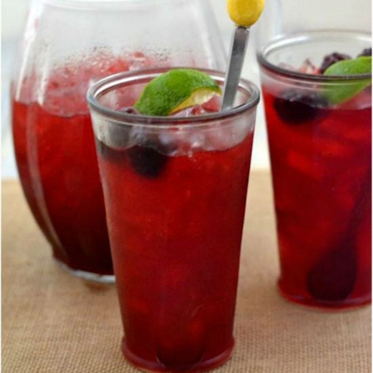 Two glasses and a pitcher filled with blackberry limeade.