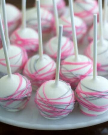 Pink and grey cakeball pops on a white cake stand.