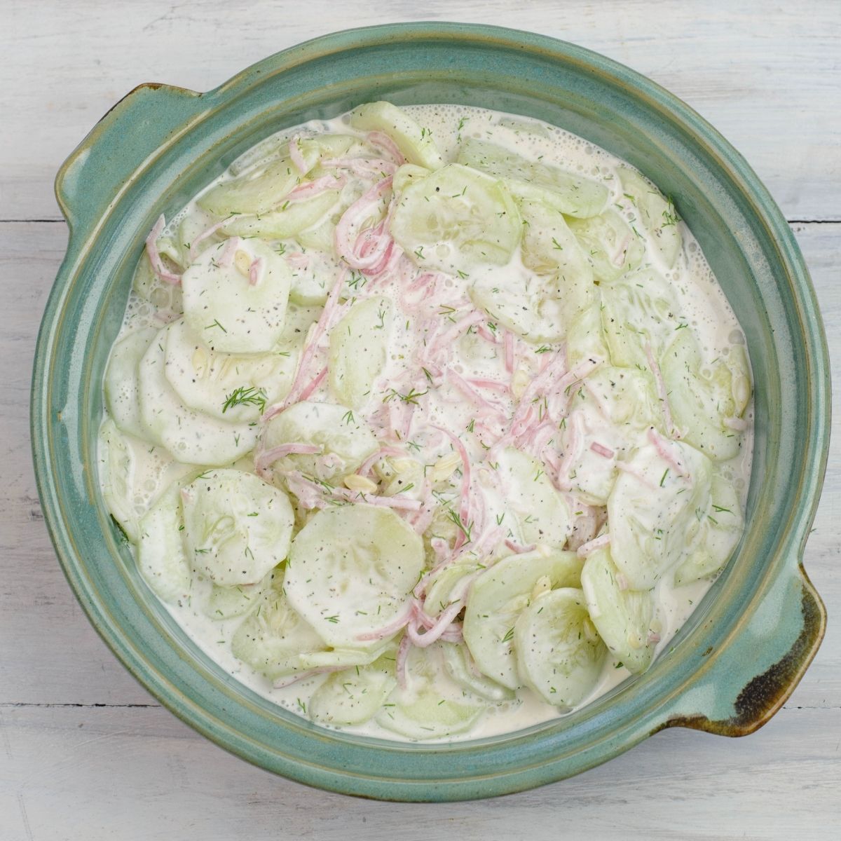 A ceramic serving bowl filled with a creamy cucumber salad.