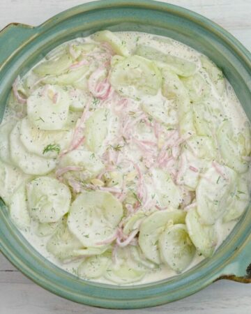 A ceramic serving bowl filled with a creamy cucumber salad.