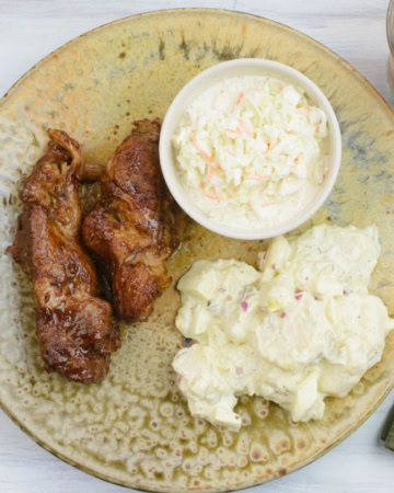 Country style pork ribs on a brown dinner plate with potato salad and coleslaw.