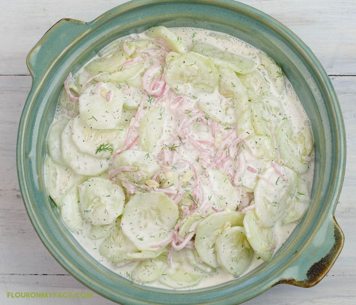 Overhead photo of a ceramic bowl filled with a creamy cucumber and red onion salad.