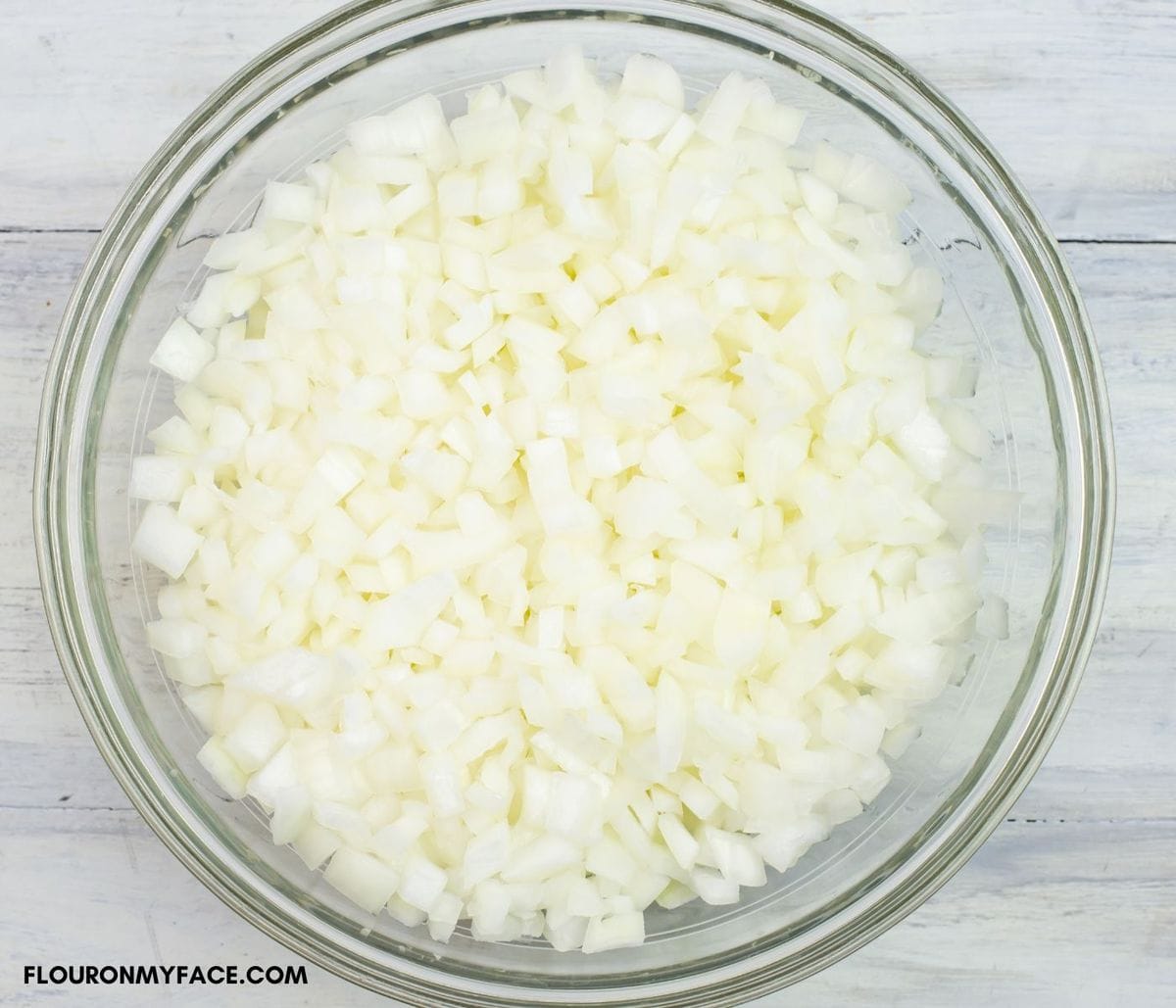 A large glass bowl filled with diced onions.