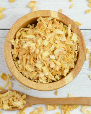 Overhead photo of a small wooden bowl and spoon filled with dehydrated onion flakes.