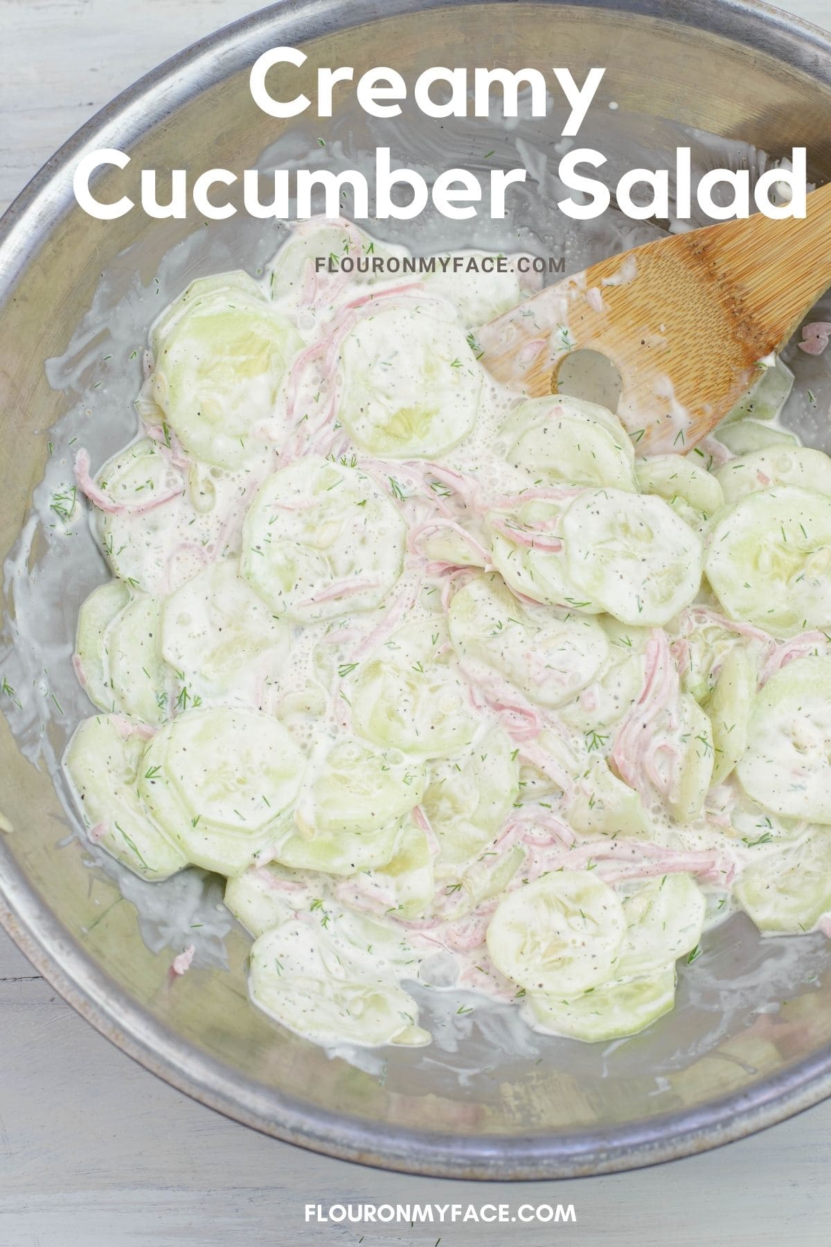 Vertical image of a metal mixing bowl filled with cucumber salad.