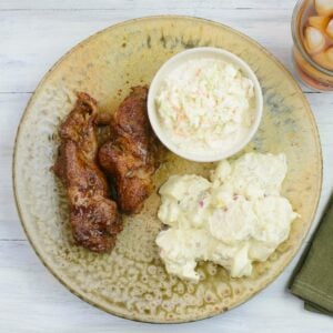 Country style pork ribs on a brown dinner plate with potato salad and coleslaw.