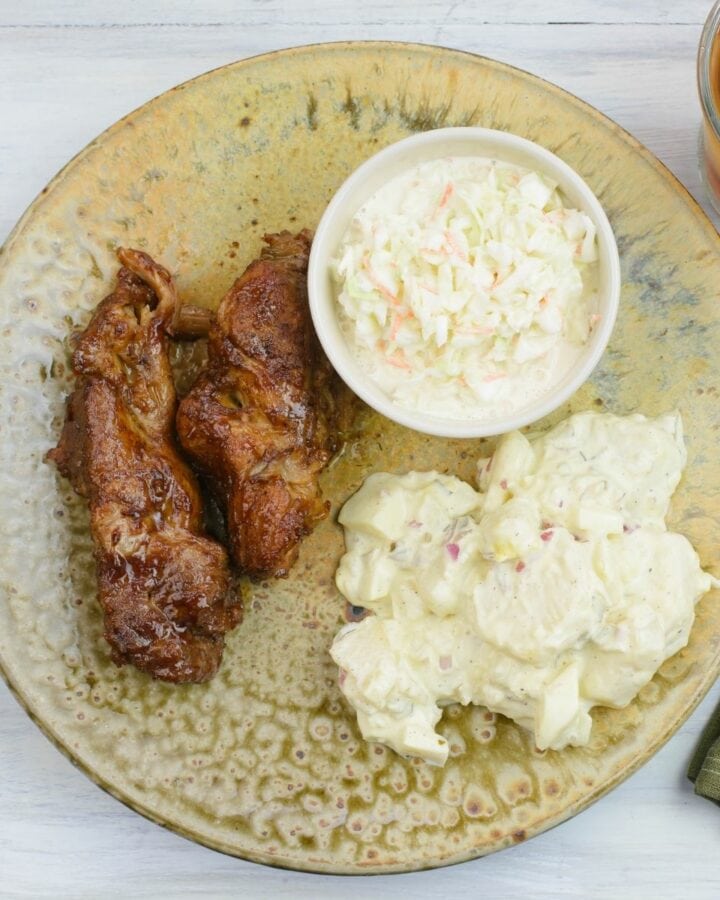 Country style pork ribs on a brown dinner plate with potato salad and coleslaw.