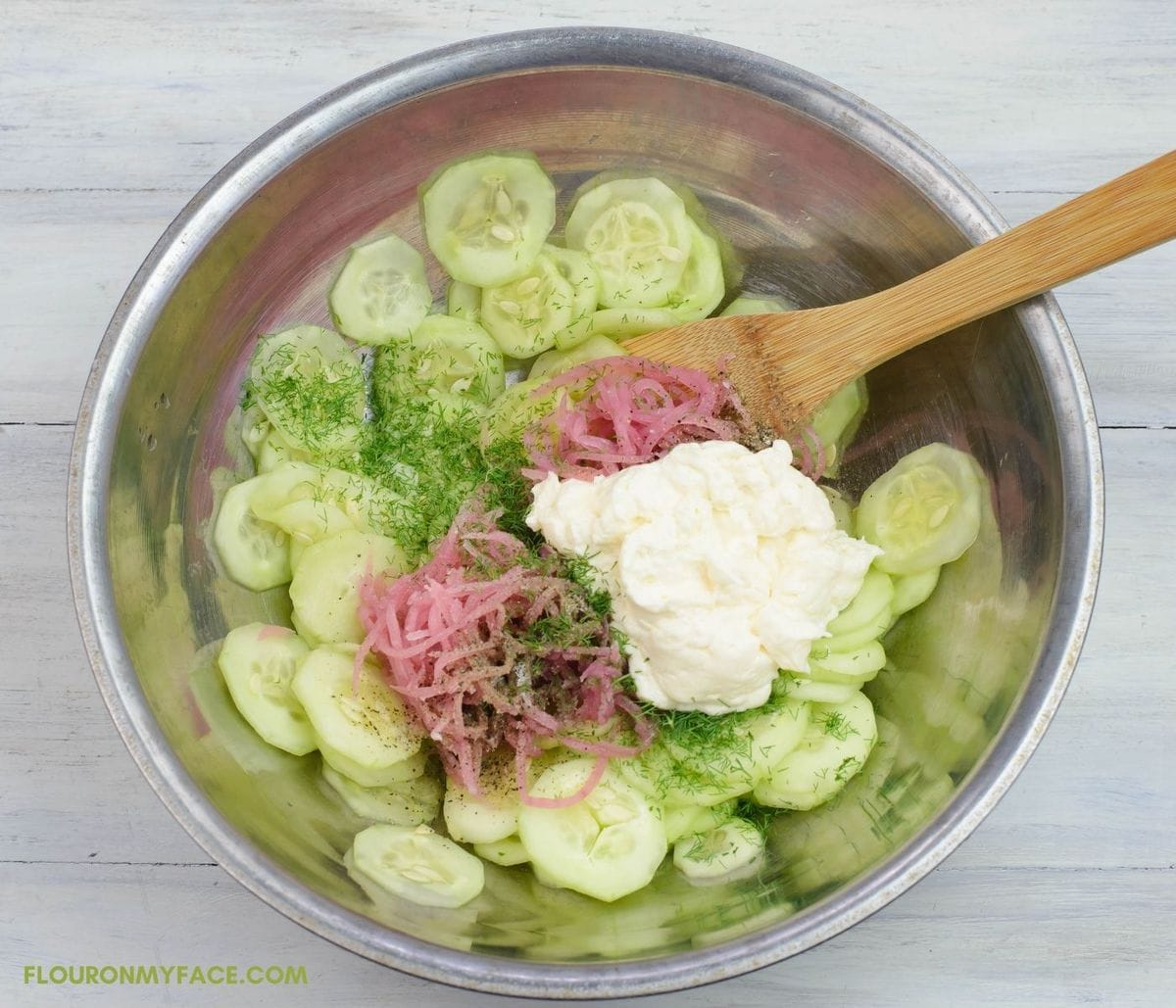 A mixing bowl filled with cucumber and onion salad before mixing the ingredients.
