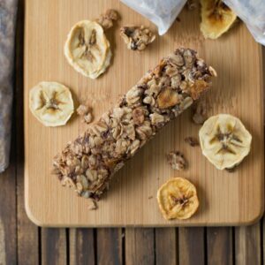 Banana Choclate Chip Granola bars on a wooden cutting board surrounded with dried banana chips.