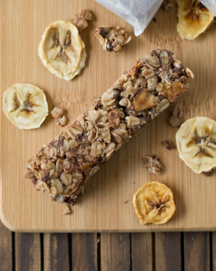 Banana Choclate Chip Granola bars on a wooden cutting board surrounded with dried banana chips.