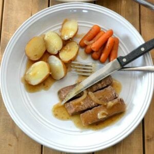 A dinner plate with a serving of crock pot London Broil with potatoes and carrots.