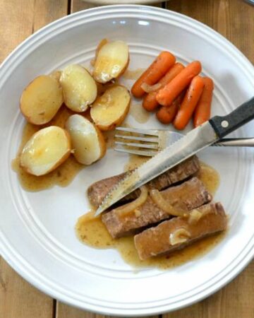A dinner plate with a serving of crock pot London Broil with potatoes and carrots.