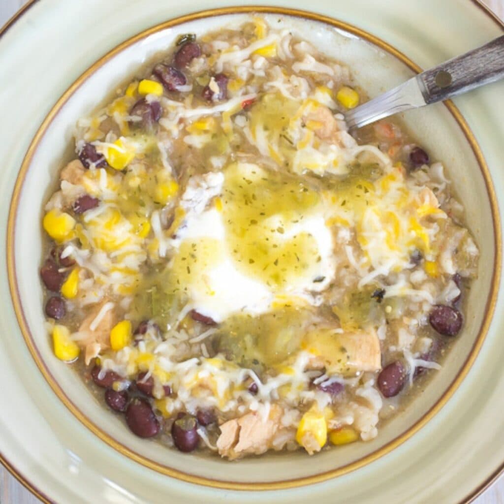 A bowl filled with garlic lime chicken salsa soup topped with sour cream and salsa verde.