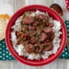 Serving red beans and rice in a red bowl on a teal napkin.